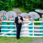 wedding photography of the bridal party standing in front of a white wooden farm gate