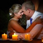 Bride and groom sitting by a table at night lit by candles on the table