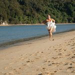 bare footed bride running away from groom on the beach