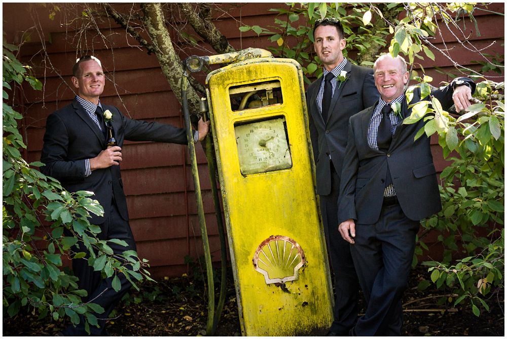 Groom-groomsmen standing by vintage petrol pump at Tipapa Woolshed